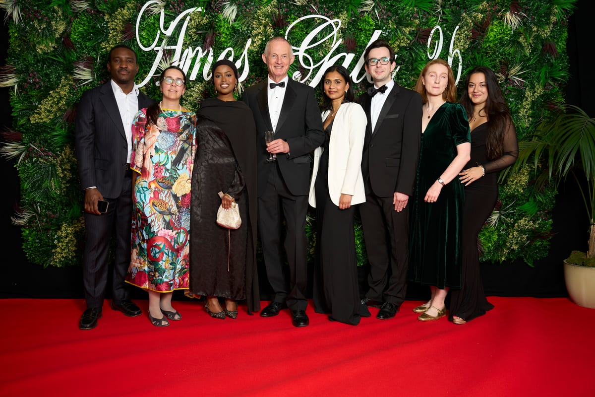 Eight guests in evening dress line up on the red carpet in front of the Amos Gala sign and a wall of greenery