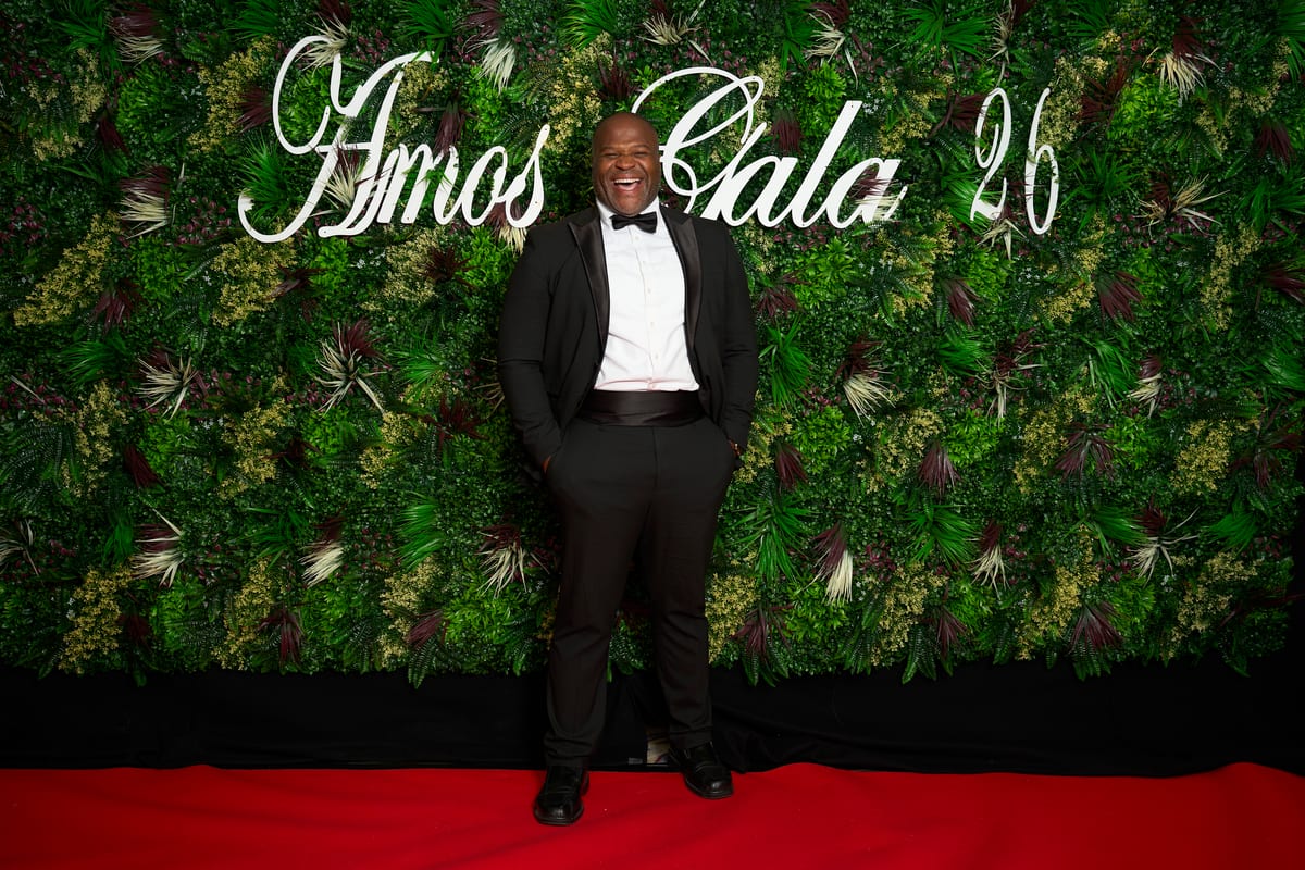 A guest in black tie laughs on the red carpet in front of the Amos Gala floral wall