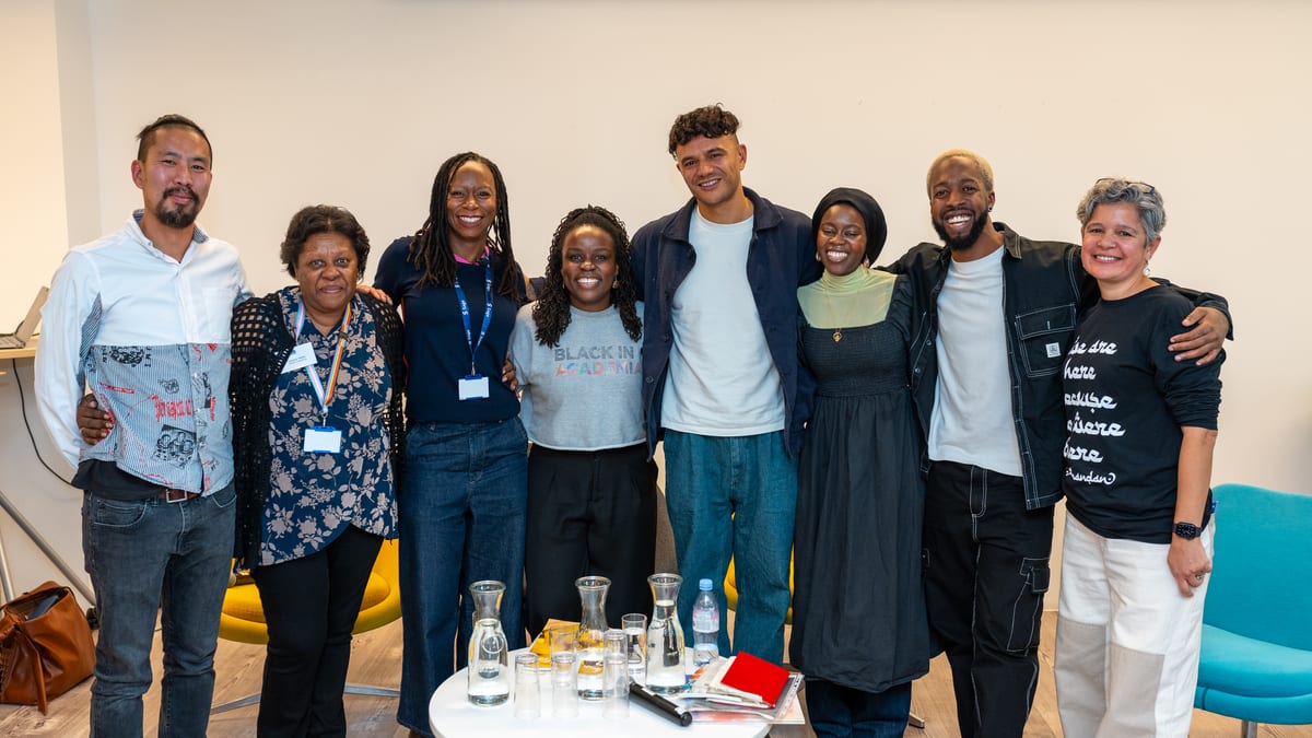 Eight speakers and organisers stand arm in arm, smiling, after a panel discussion at a community event