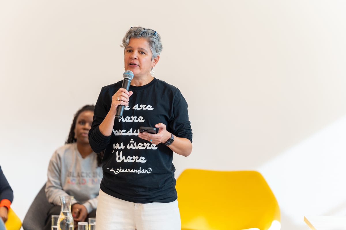 A speaker in a slogan T-shirt addresses the audience with a microphone during a community panel discussion
