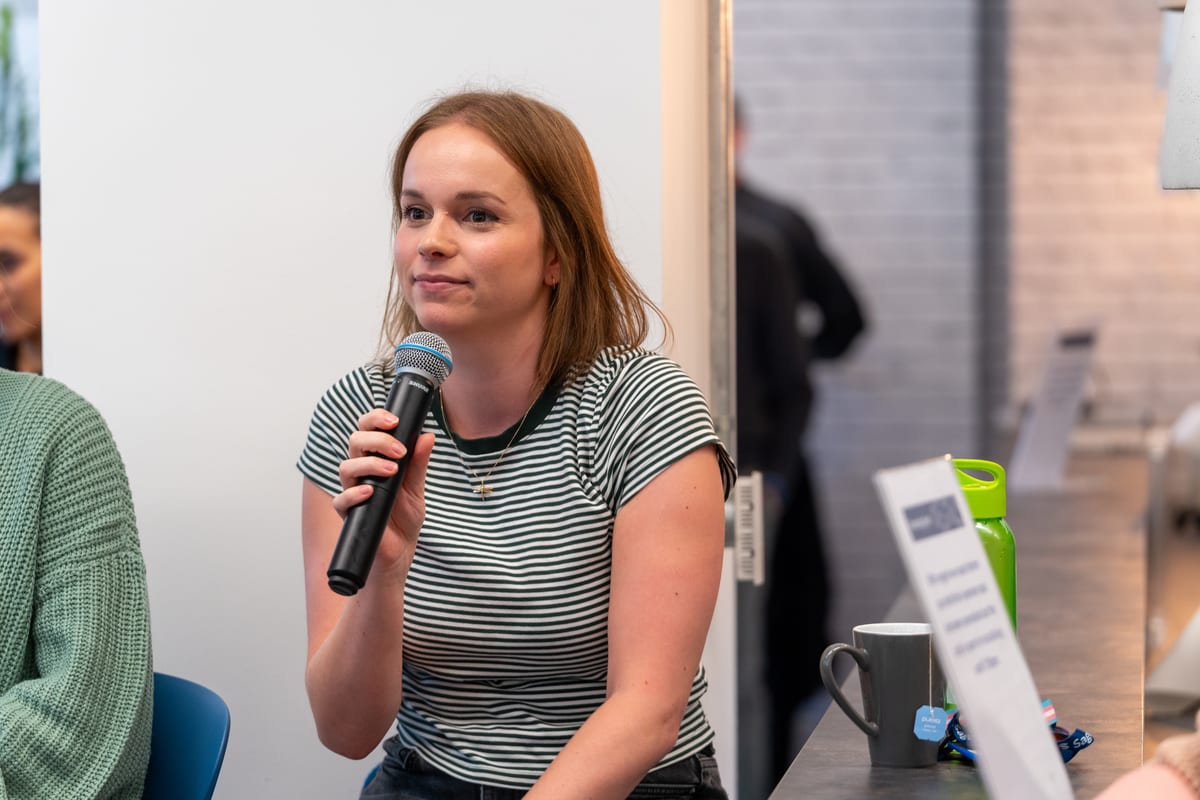 A young woman in a striped T-shirt speaks into a microphone during a panel discussion